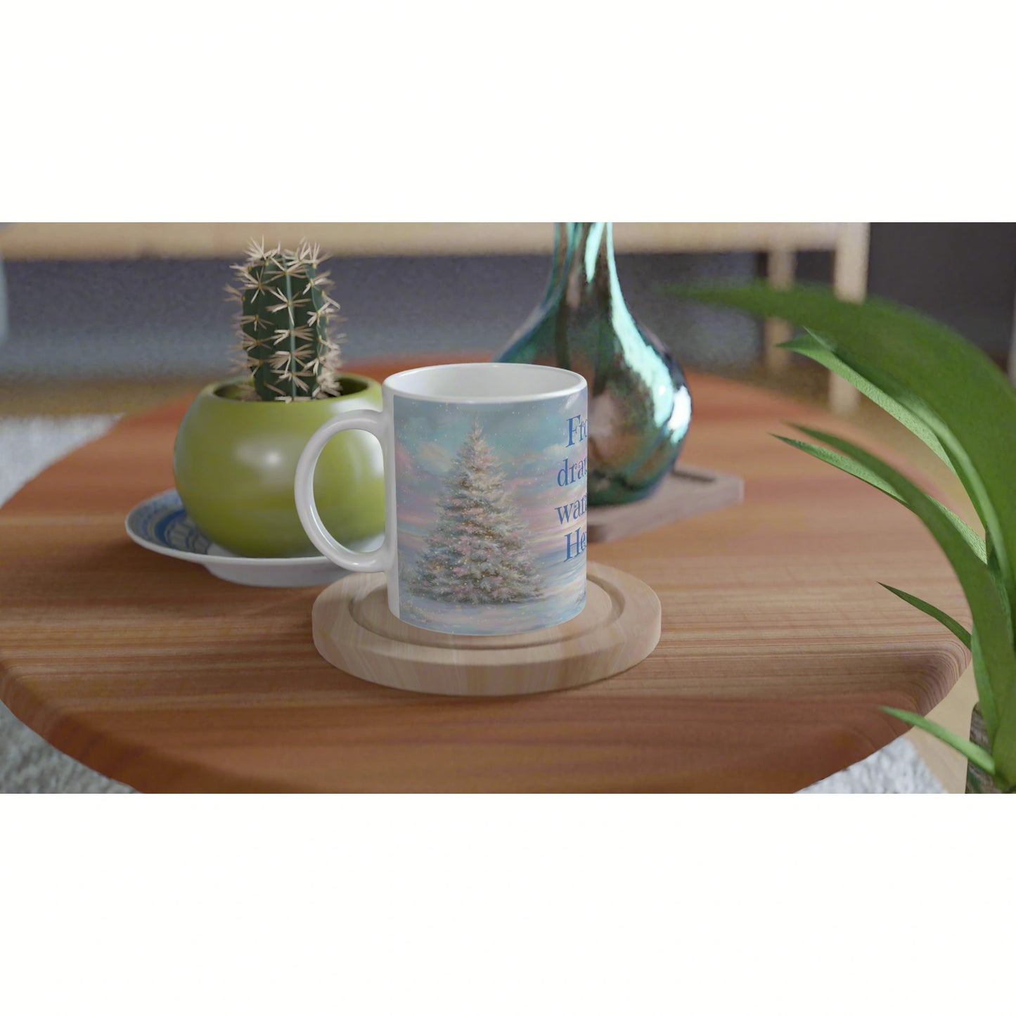 White mug featuring a snowy Christmas tree scene on a wooden table, with potted cactus and green vase in the background.