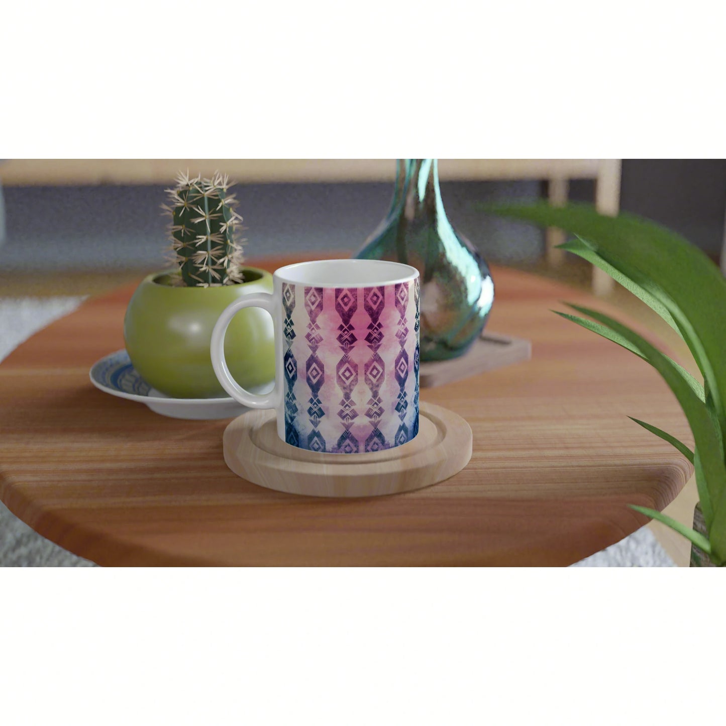 Product mockup: white ceramic mug with blue-to-pink geometric gradient on a wooden table, beside a cactus and leafy plant.