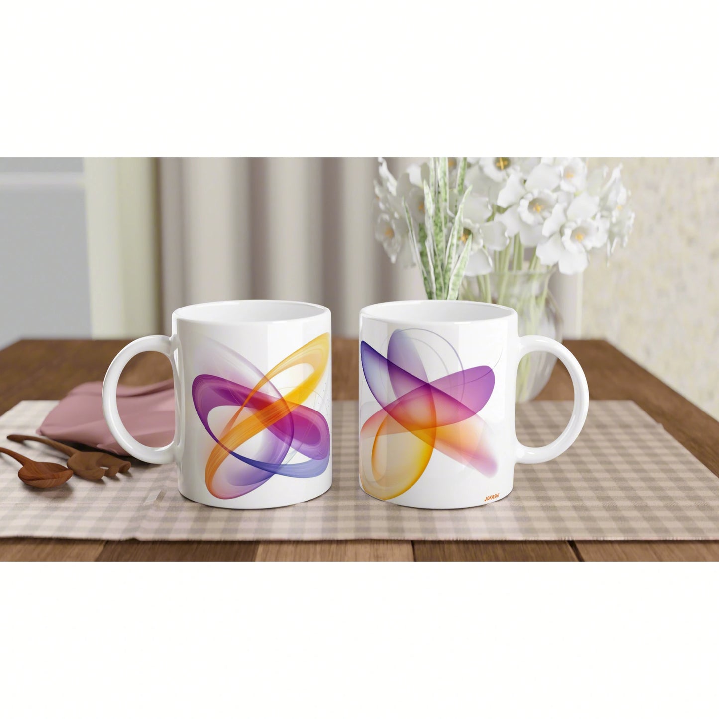 Two white ceramic mugs with colorful abstract swirl designs on a wooden table; blurred white flowers in the background.