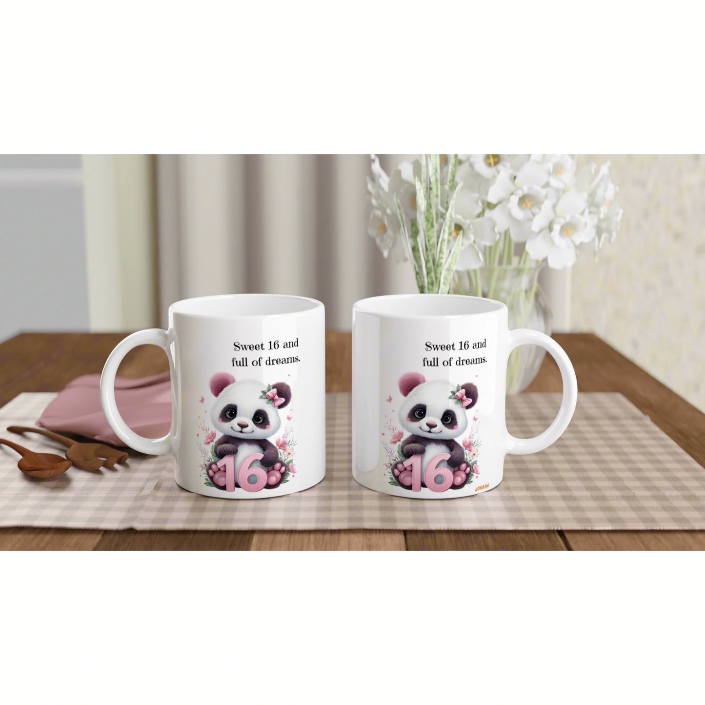 Two white mugs with panda illustration and Sweet 16 and full of dreams text, displayed on a table with a vase of white blooms