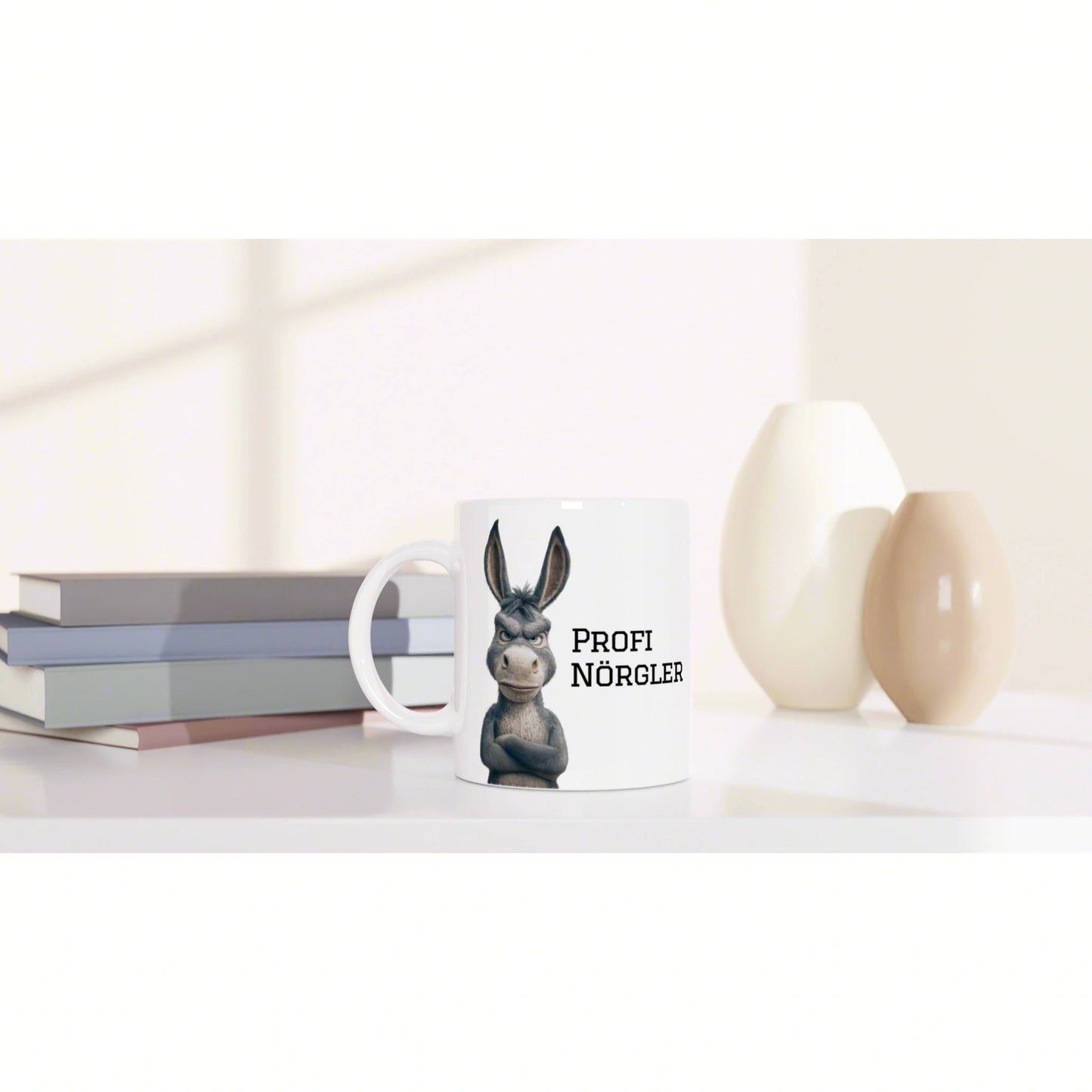 White mug mockup featuring a cartoon donkey and bold text, placed beside stacked books and decorative white and beige ceramic vases.