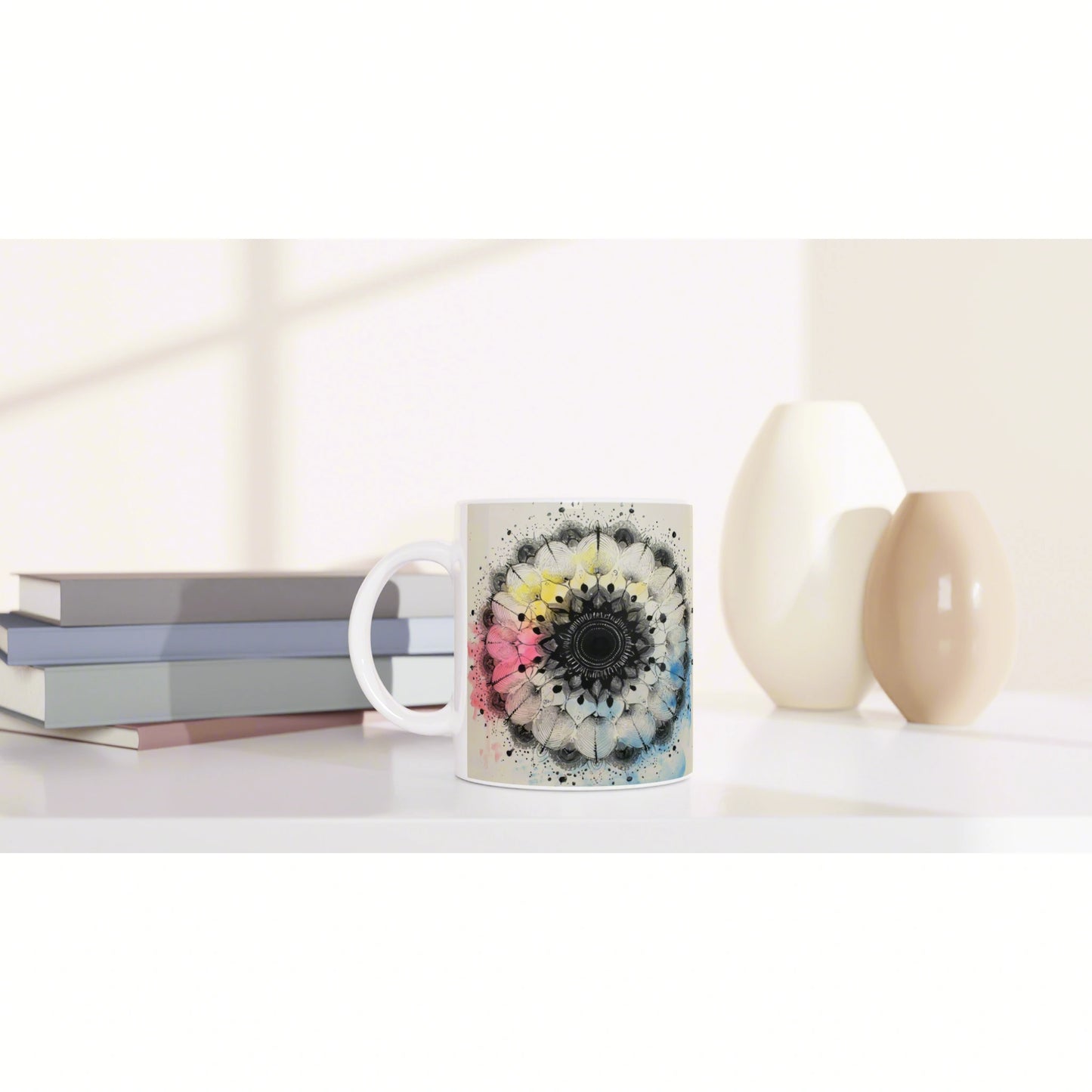 White mug with a colorful mandala floral design on a white shelf beside pastel books and ceramic vases—product mockup.