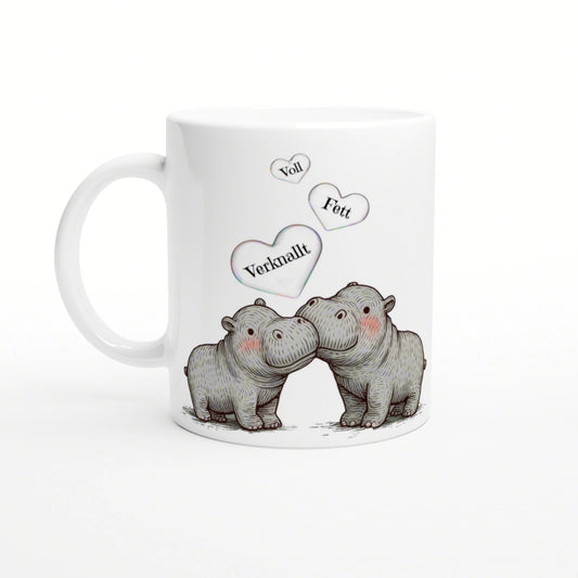 White mug with a sketch of two cuddling hippos and three floating hearts labeled Voll, Fett, Verknallt.