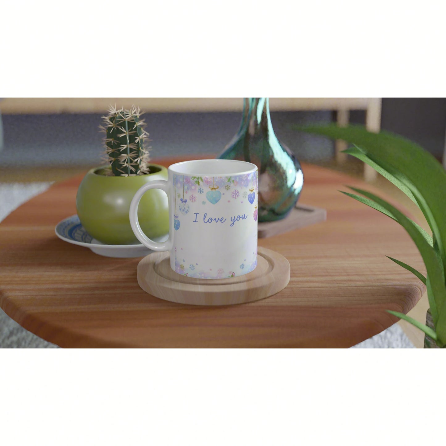 White mug with pastel heart decorations and I love you text on a wooden coaster, on a table with a cactus pot.