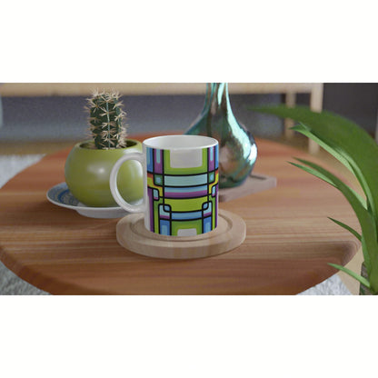 Colorful geometric-pattern mug on a wooden table, with a cactus plant and decorative vase in the background; product mockup.
