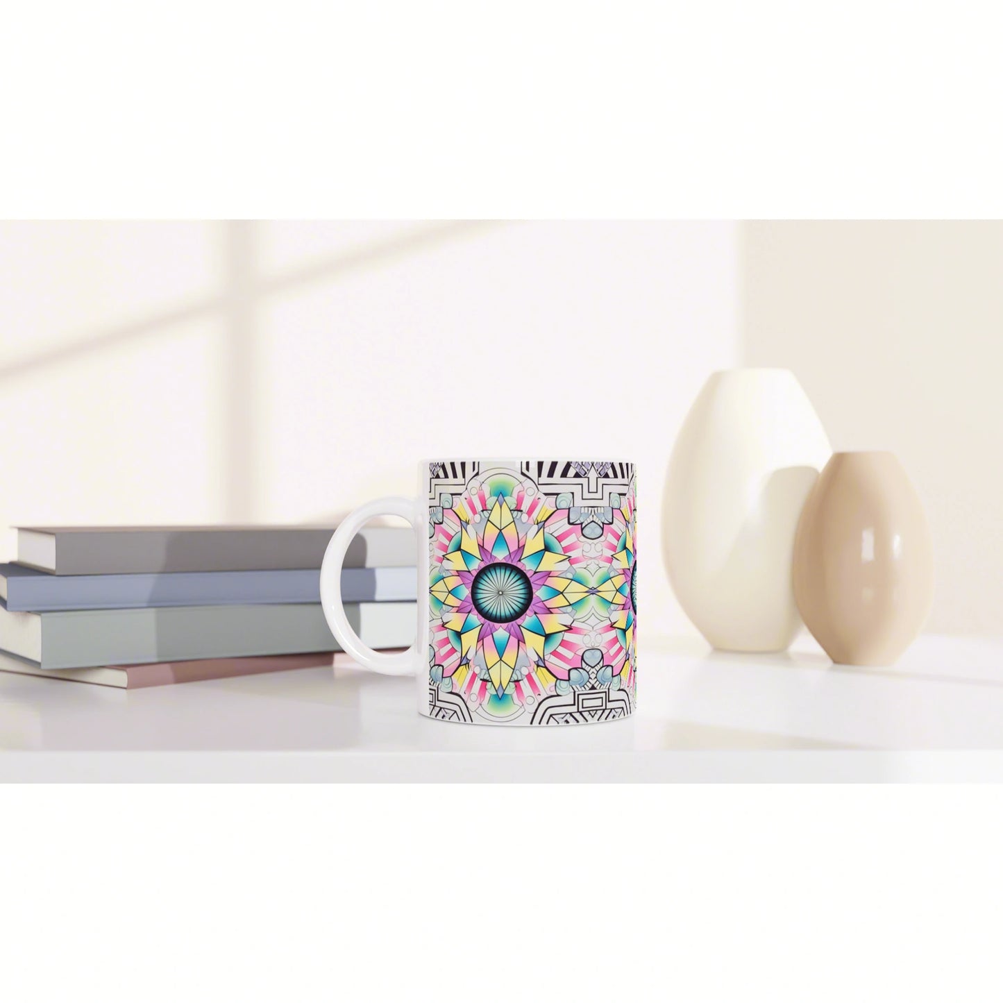 Colorful mandala-pattern mug mockup on a white desk, with a stack of books and decorative vases in the background.