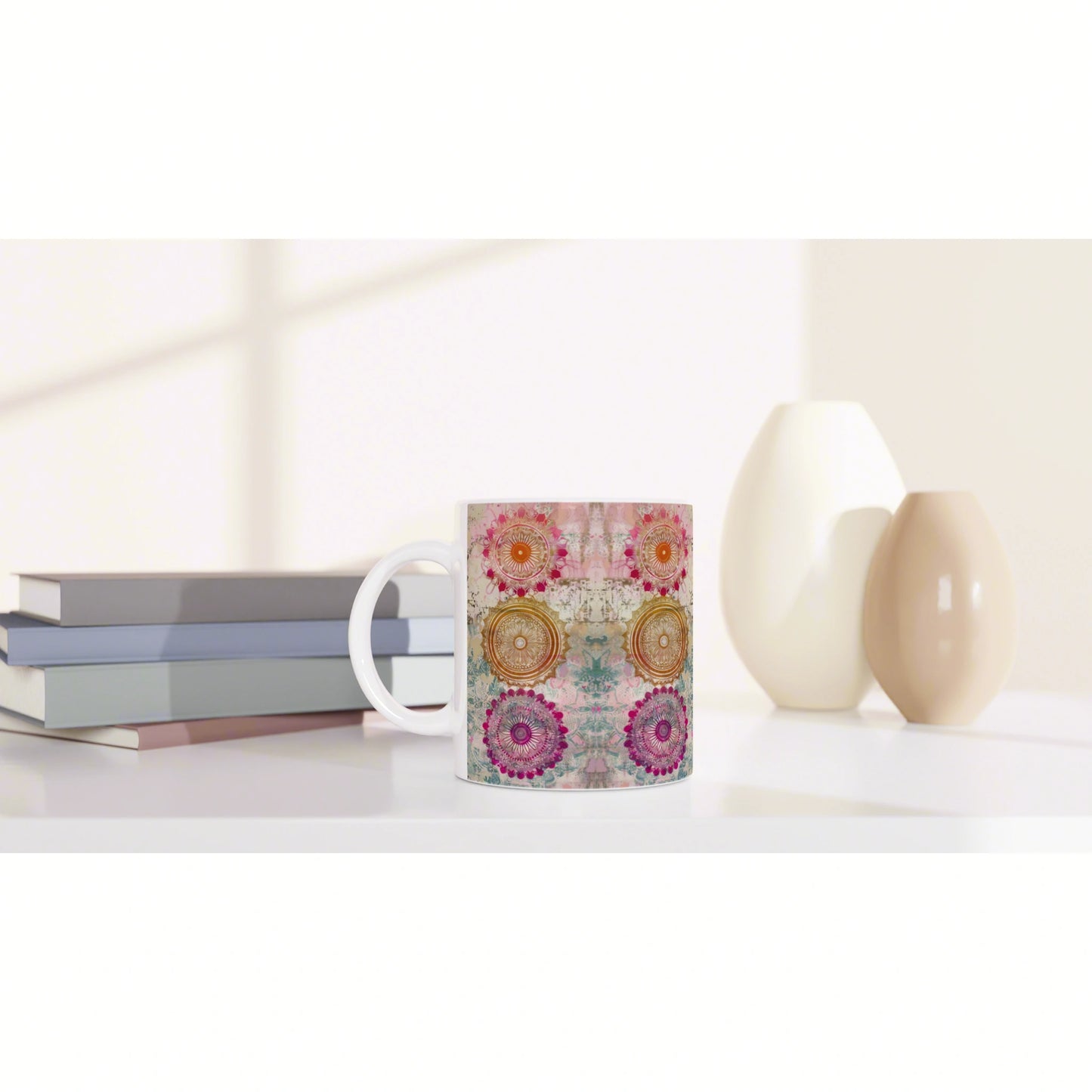 Colorful mug with circular mandala patterns on a white background, shown with books and ceramic vases in a studio mockup.