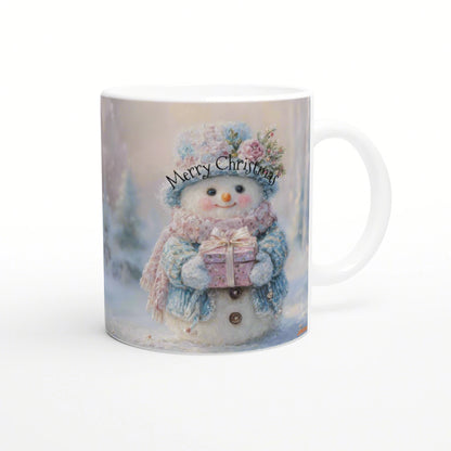 White mug featuring a cute snowman wearing a blue hat and scarf, holding a pink gift, with 'Merry Christmas' text in a snowy background.