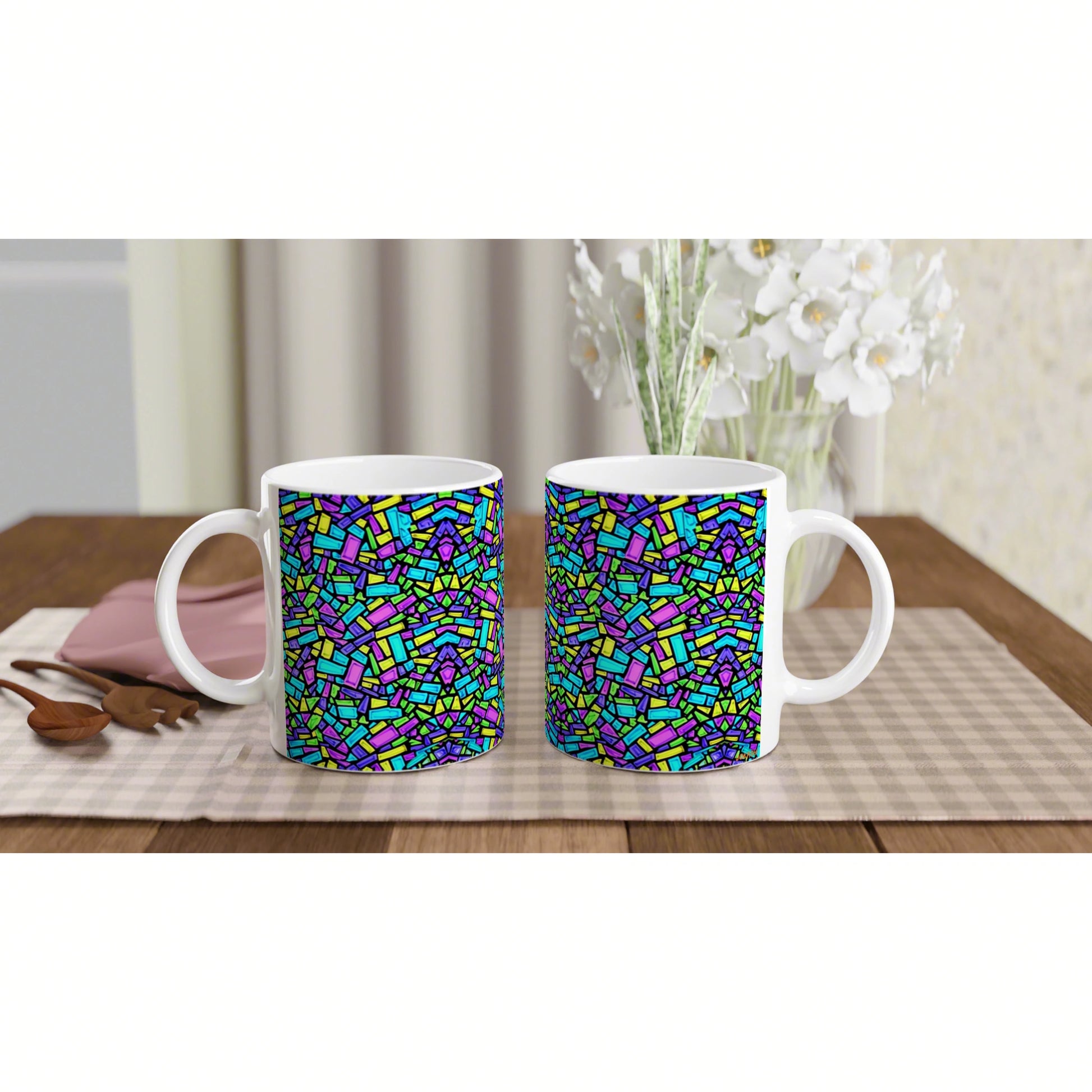 Mockup: two white ceramic mugs with a multicolor mosaic pattern on a wooden table, checkered placemat, and white flowers.