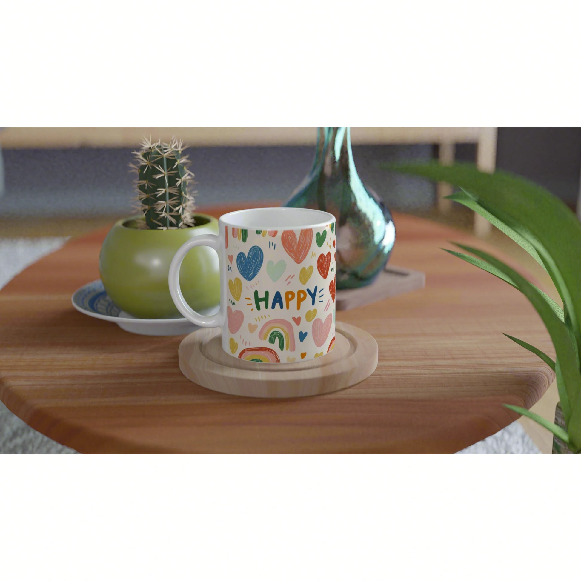 Product mockup: white mug with colorful hearts and the word HAPPY on a wooden table, next to a cactus pot and glass vase.