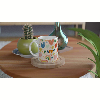Product mockup: white mug with colorful hearts and the word HAPPY on a wooden table, next to a cactus pot and glass vase.