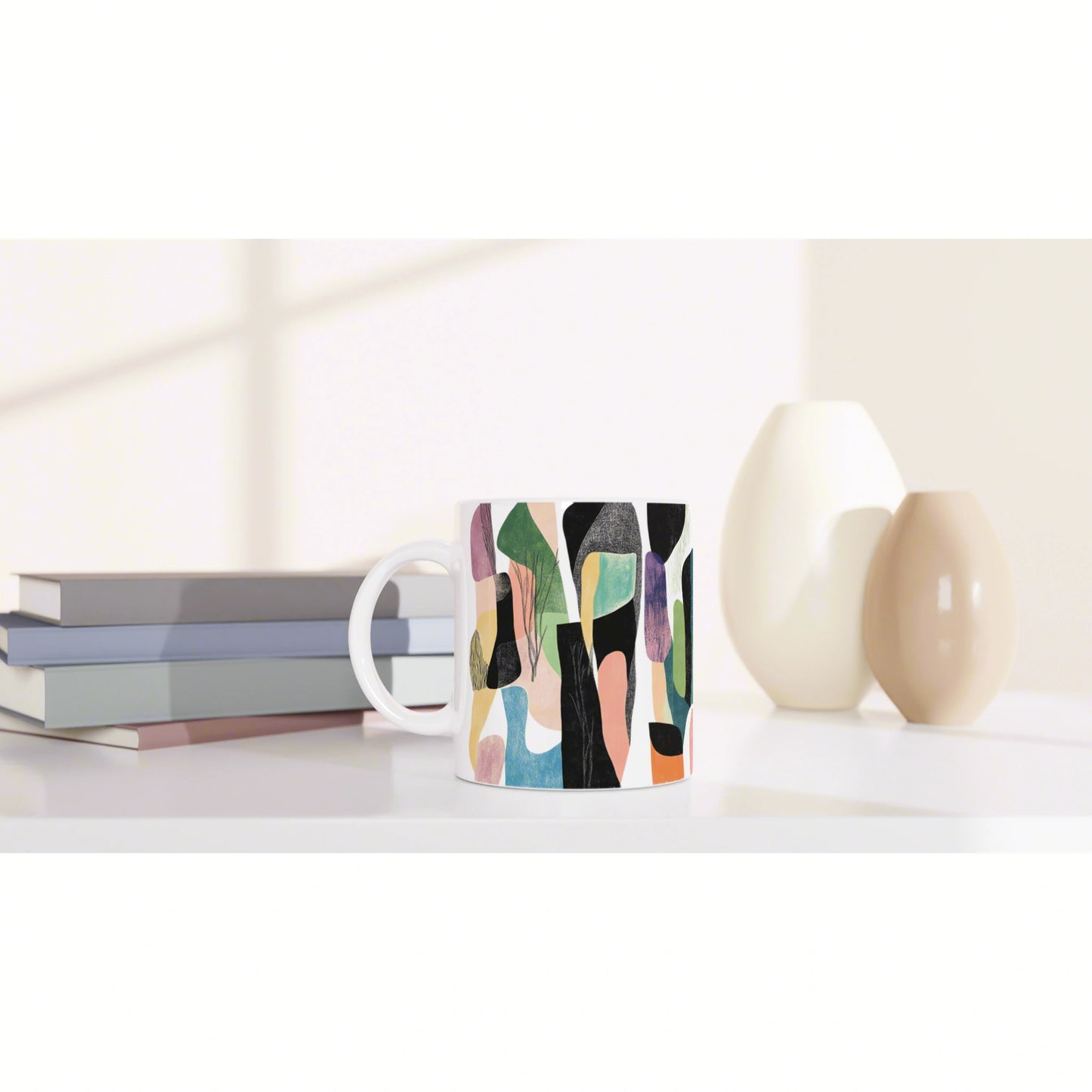 Mug with an abstract colorful pattern on a white desk, beside stacked books and pastel vases (product mockup).