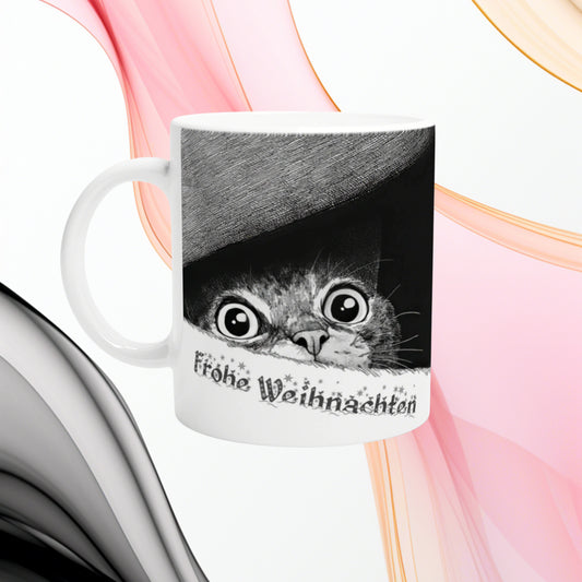 Product mug mockup: white ceramic cup featuring a black-and-white illustration of a wide-eyed cat peeking from under a hat, with 'Frohe Weihnachten' text.