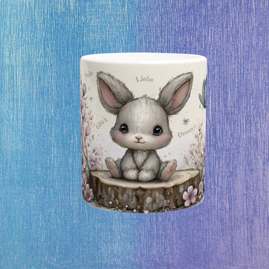 White ceramic mug featuring a cute gray bunny sitting on a tree stump, surrounded by pastel flowers; product mockup.