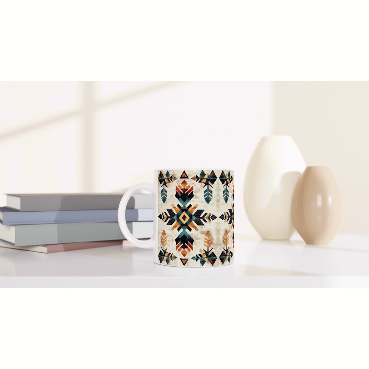 Mug with geometric tribal pattern in teal, orange, and black on a white surface; books on the left and ceramic vases on the right.