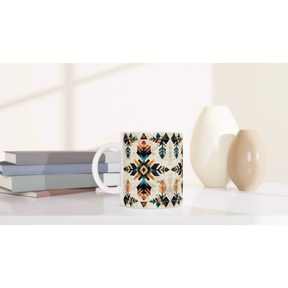 Mug with geometric tribal pattern in teal, orange, and black on a white surface; books on the left and ceramic vases on the right.