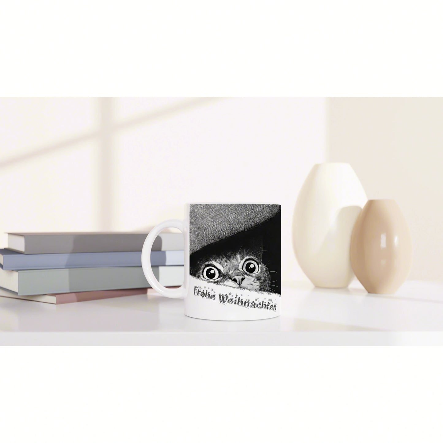 Mug mockup with a black-and-white kitten peeking from under a hat and Frohe Weihnachten text, beside books and vases.