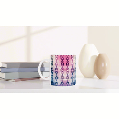 Mug featuring a pink-to-purple geometric pattern sits on a white desk beside pastel books and two ceramic vases.