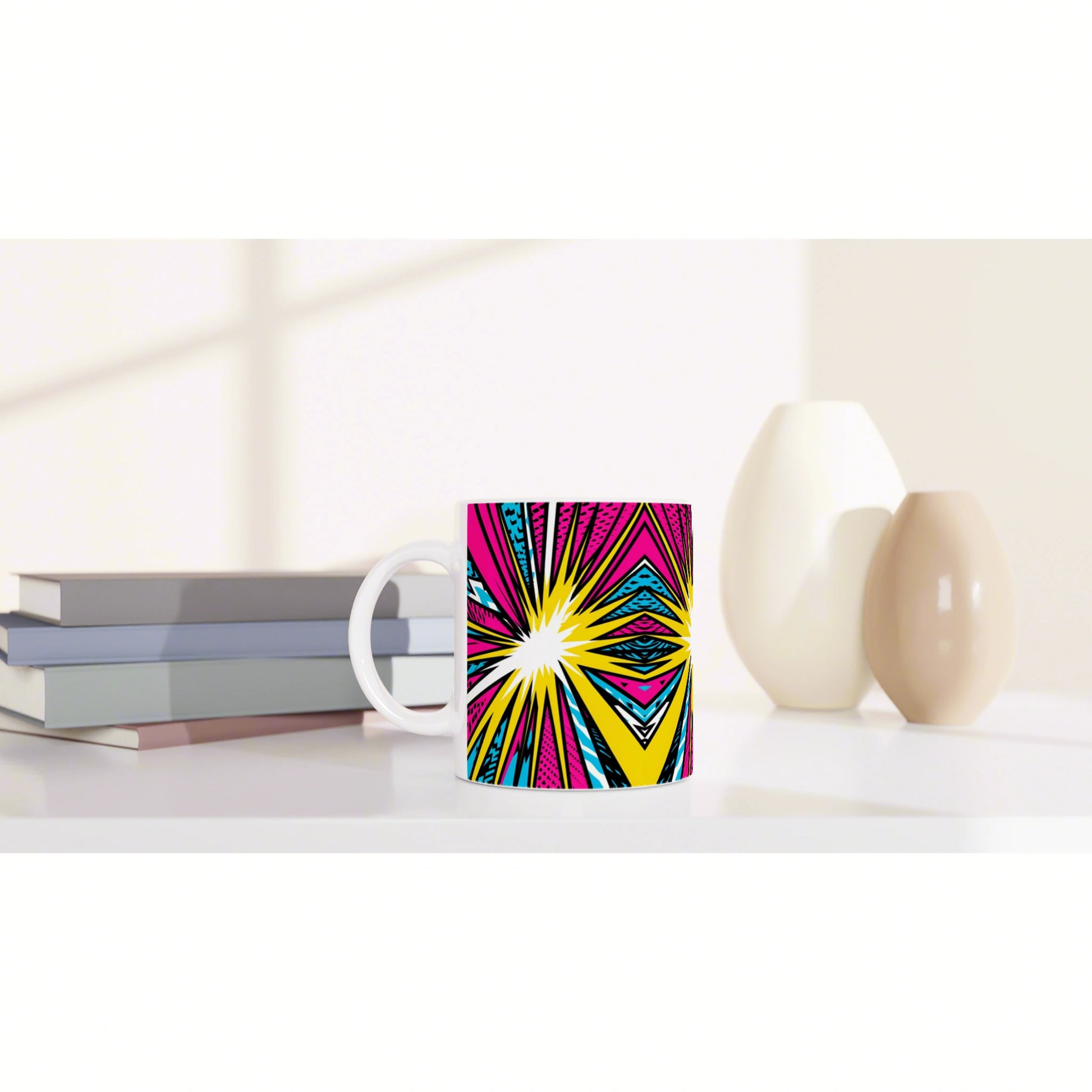 Bright mug with a pink-yellow-blue pop-art starburst pattern on a white desk beside stacked books and ceramic vases.