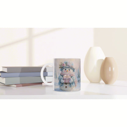 Mug featuring a snowy snowman and 'Merry Christmas' text, placed on a desk with books and decorative vases in soft lighting.