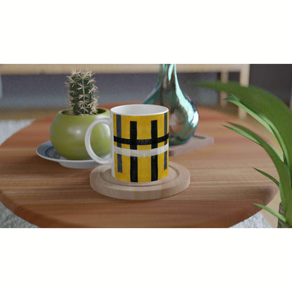 Mug with yellow, black and white geometric pattern on a wooden coaster, on a table with a cactus and plant.