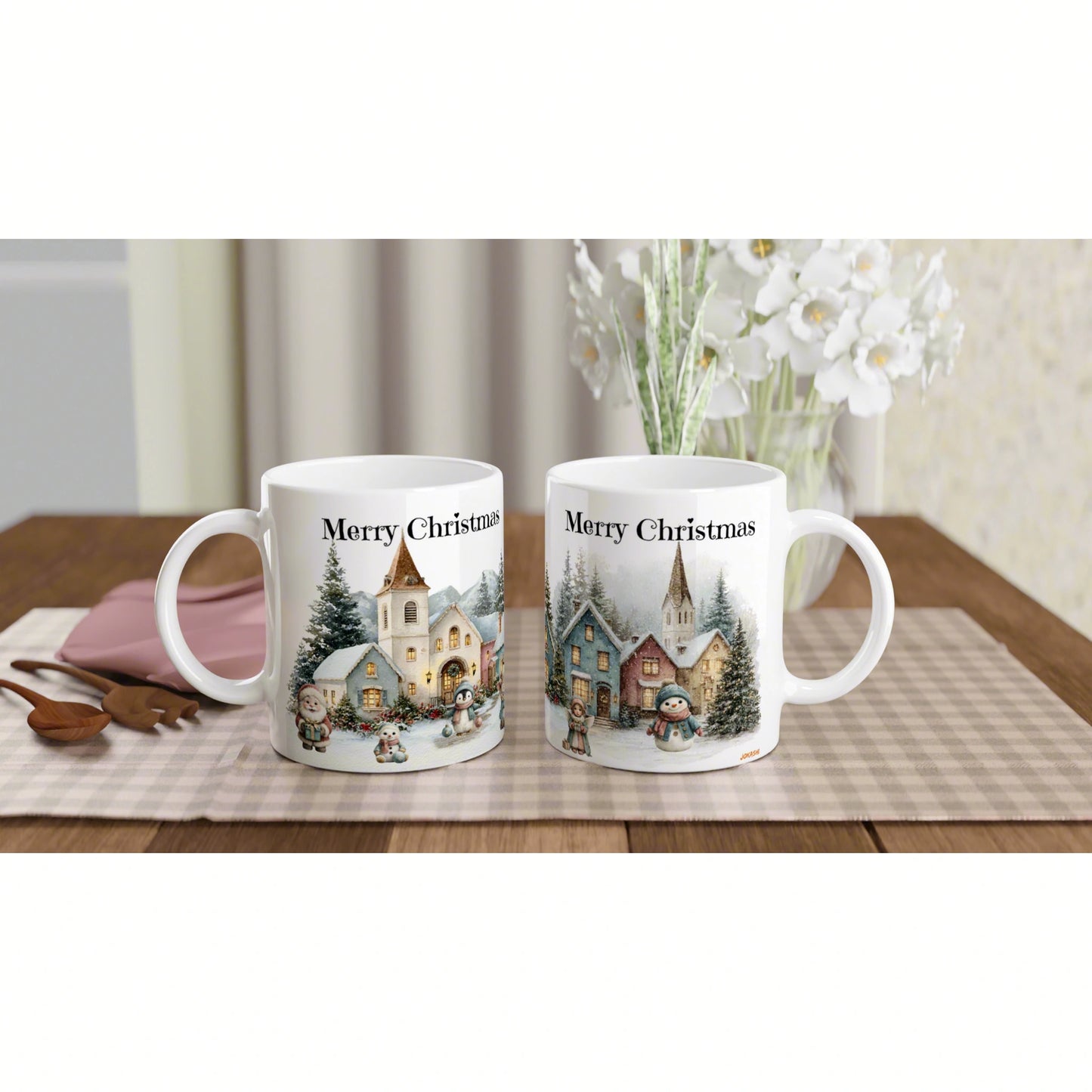 Pair of white mugs with 'Merry Christmas' and snowy village scenes on a checkered table runner.