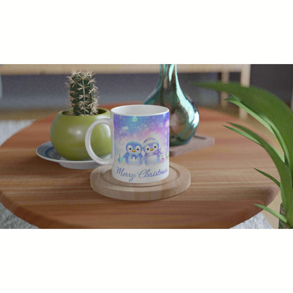 Product mockup: white mug with pastel penguin Christmas scene and 'Merry Christmas' text on a wooden table with nearby plants.