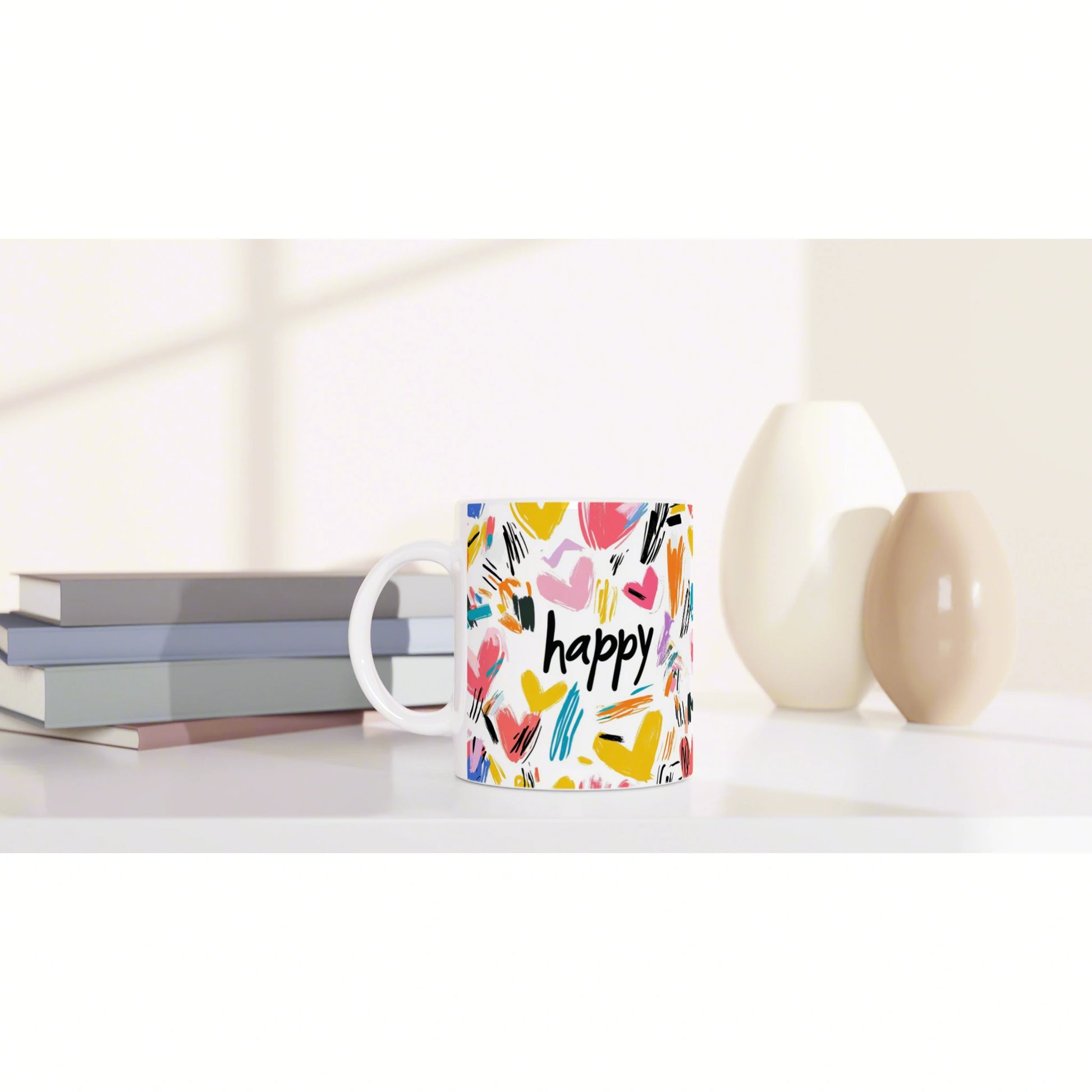 Product mockup: colorful mug with happy and brushstroke heart pattern, shown on a desk with books and ceramic vases.