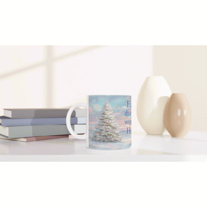 Product mockup: mug with snowy Christmas tree print on a white shelf, flanked by pastel books and two neutral vases.