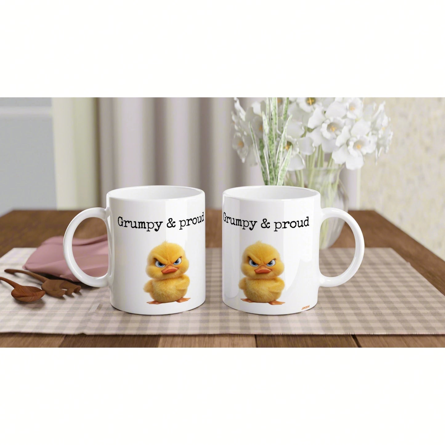 Product mockup: two white mugs with 'Grumpy & proud' and a yellow chick, on a wooden table.