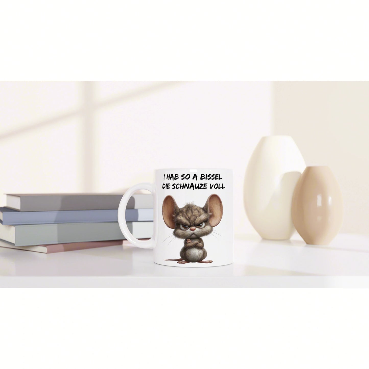 Product mockup: white mug with an angry cartoon mouse and a German slogan, set on a desk beside books and decorative vases.
