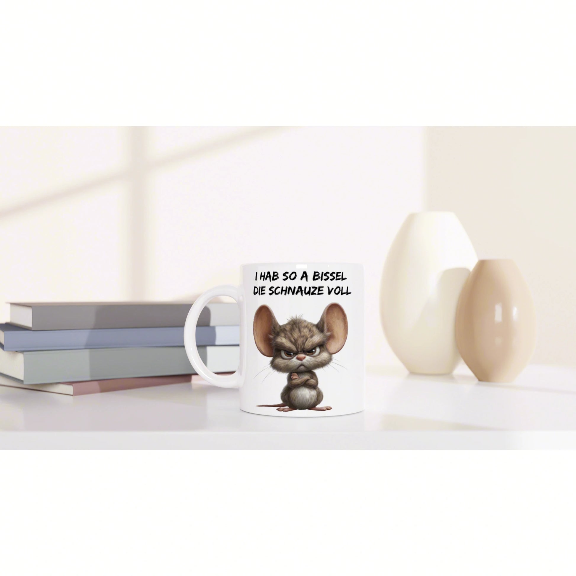 Product mockup: white mug with an angry cartoon mouse and a German slogan, set on a desk beside books and decorative vases.