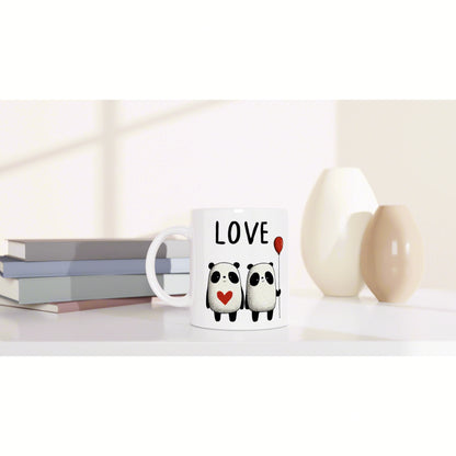 Product mockup: white mug with LOVE, two pandas, heart and balloon; background shows books and vases.