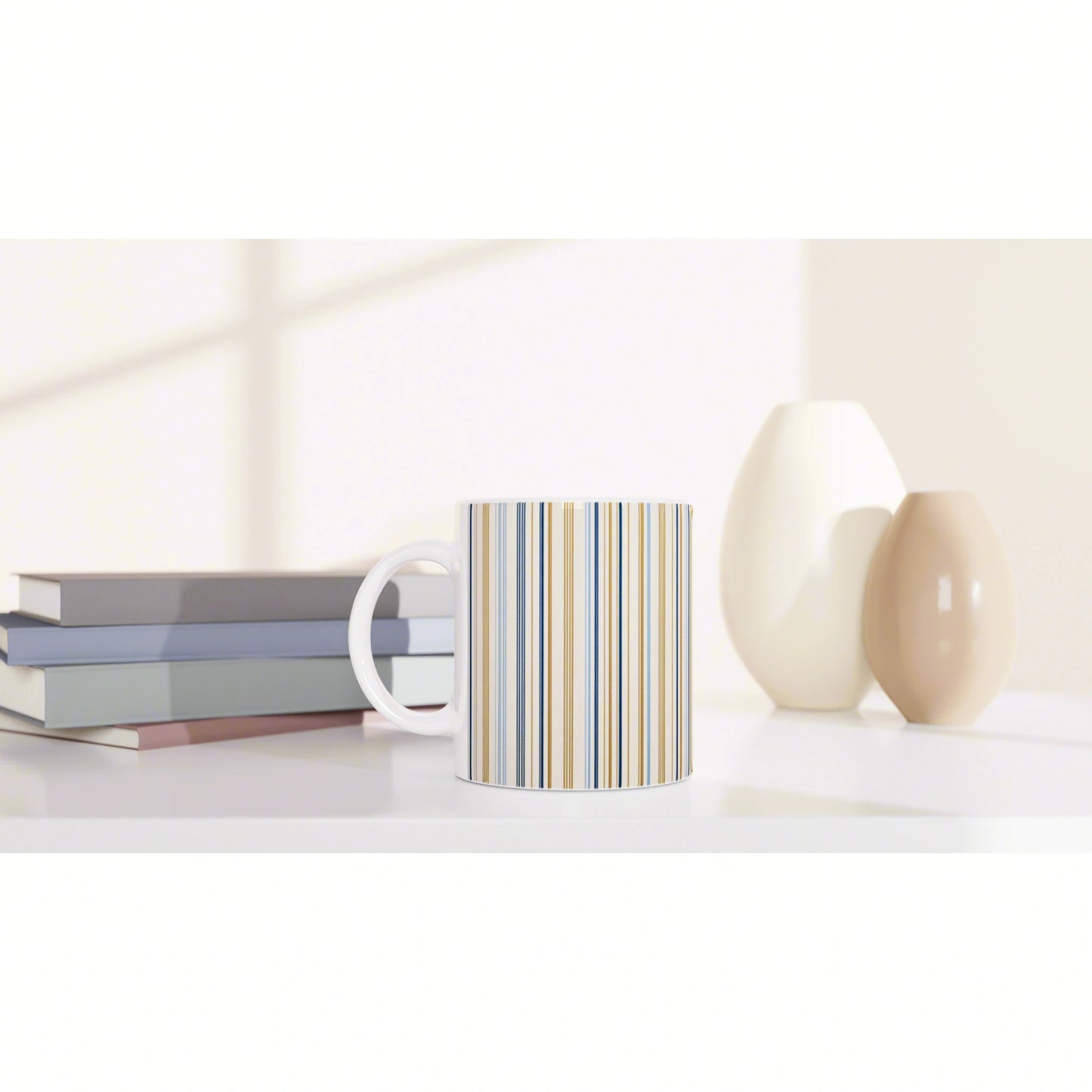 Striped ceramic mug on a white shelf beside pastel books and two cream-colored vases in a bright, minimalist still life.