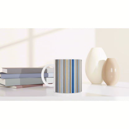 White mug with blue and beige vertical stripes on a shelf, beside a stack of books and two ceramic vases.
