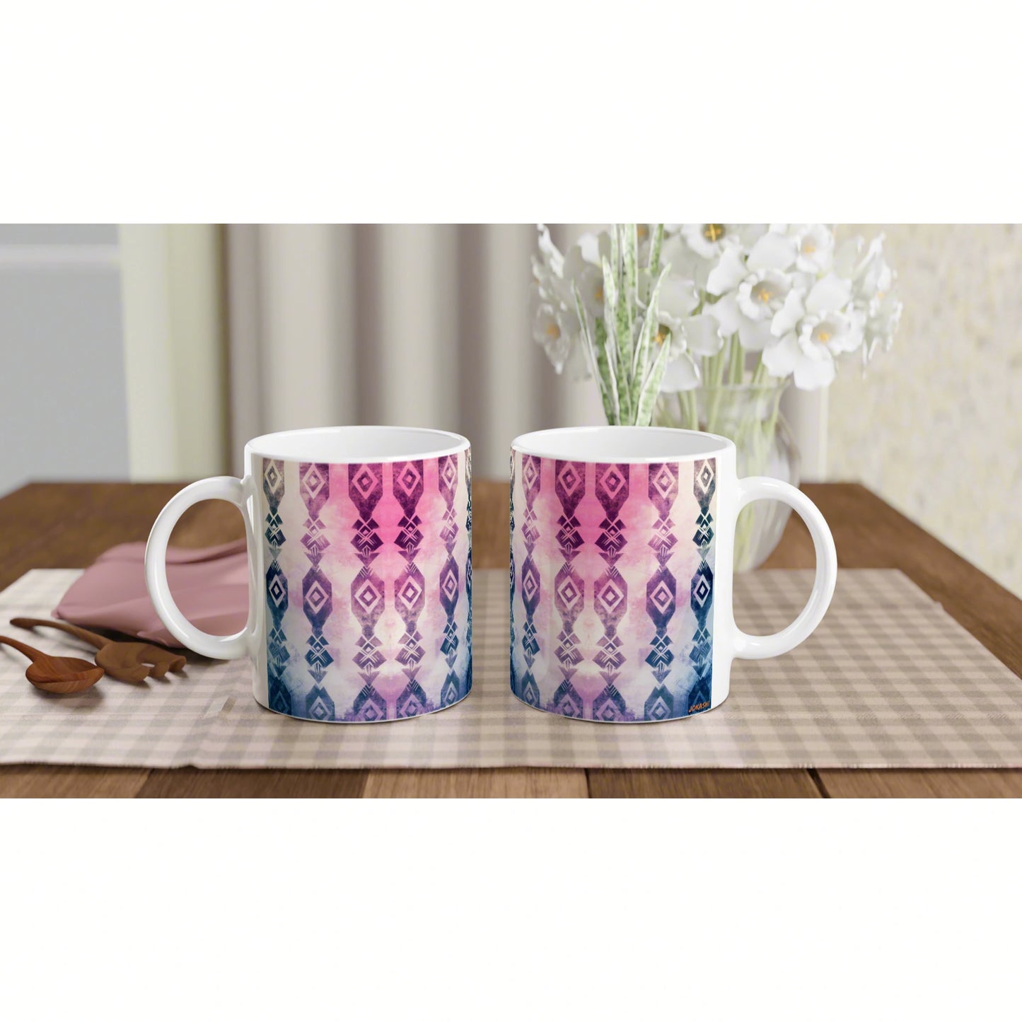 Two ceramic mugs with pink-to-blue geometric pattern on a checkered placemat, floral vase in background; product mockup.