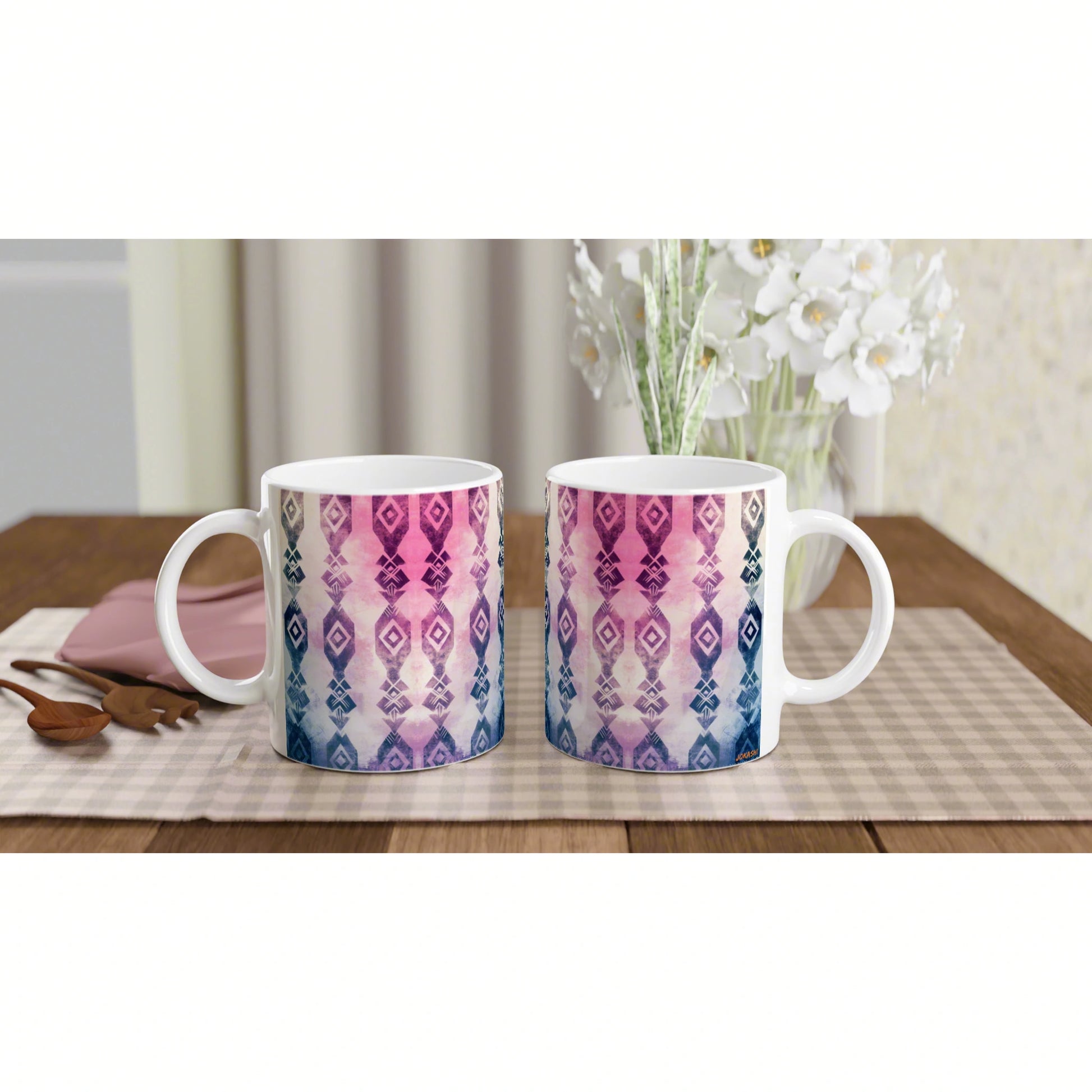 Two ceramic mugs with pink-to-blue geometric pattern on a checkered placemat, floral vase in background; product mockup.