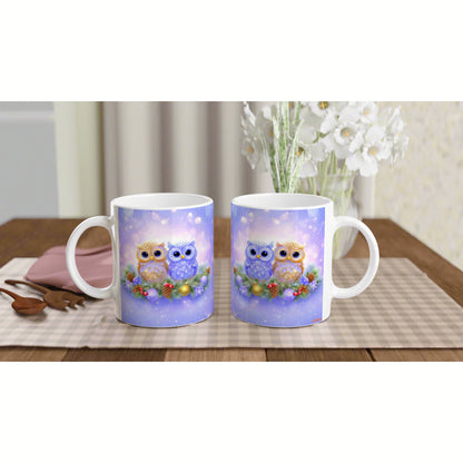 Two white mugs feature a cute owl illustration on a purple background; owls perched on a berry garland on a checkered placemat.