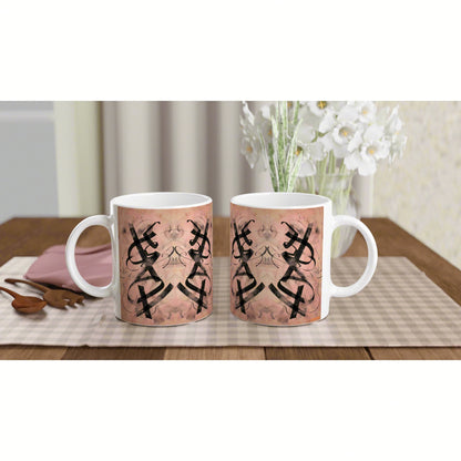 Two white ceramic mugs on a wooden table featuring a pink patterned wrap with black mirrored geometric motifs.