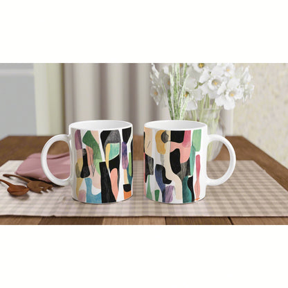 Two white ceramic mugs with abstract multicolor patterns on a beige placemat on a wooden table.