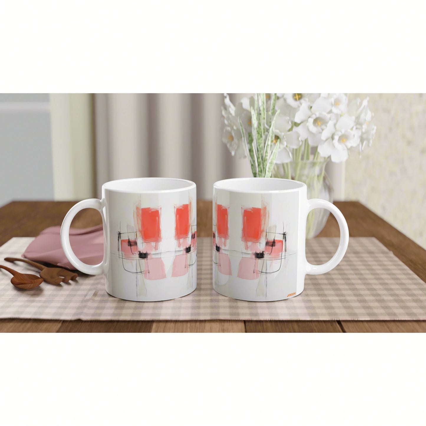Product mockup: two white ceramic mugs with abstract pink-red shapes and black lines on a checkered placemat.