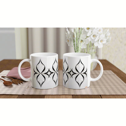 Two white ceramic mugs with black geometric floral patterns on a wooden table with a beige placemat; product mockup.