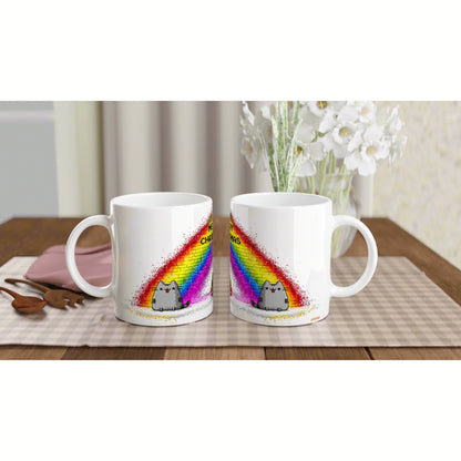 Two white ceramic mugs on a wooden table show a cartoon gray cat under a bright rainbow; a product mockup for an online shop.