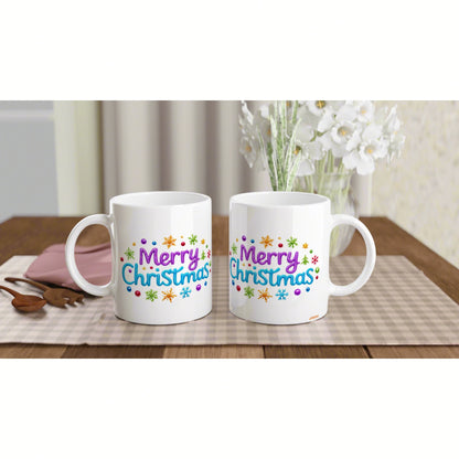 Two white ceramic mugs on a wooden table feature a colorful 'Merry Christmas' design with snowflakes.