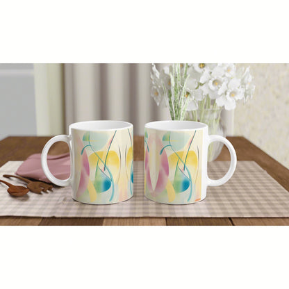 Two white ceramic mugs with pastel abstract patterns on a wooden table, plaid placemat, and white flowers in the background.