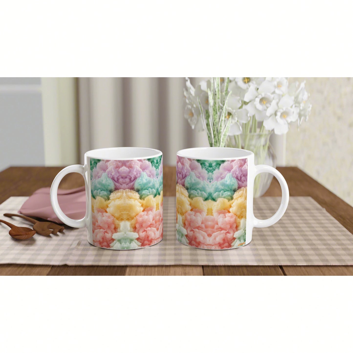 Product mockup: two white ceramic mugs with rainbow tie-dye patterns on a wooden table, with a checkered placemat and white flowers in the background.