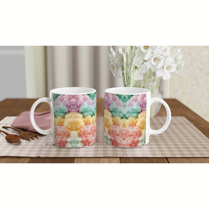 Product mockup: two white ceramic mugs with rainbow tie-dye patterns on a wooden table, with a checkered placemat and white flowers in the background.