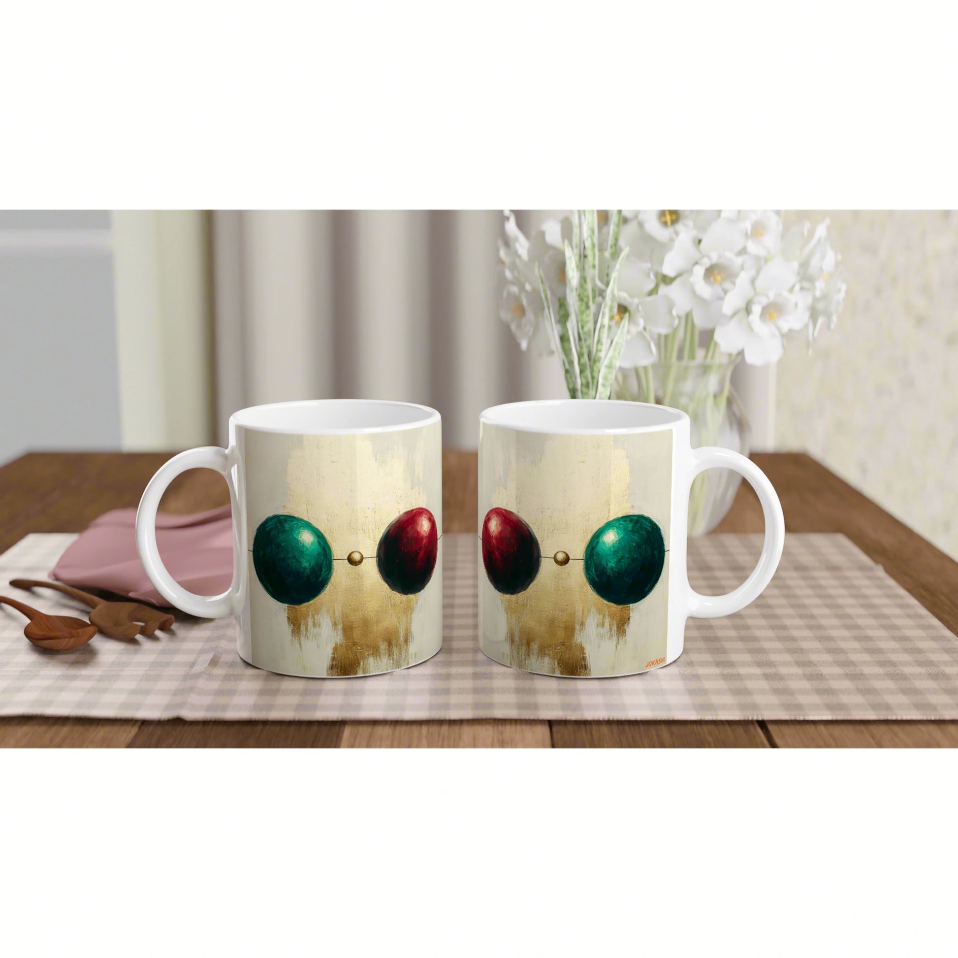 Product mockup: two white mugs with abstract gold-toned art featuring green and red spheres linked by a dot on a beige mat.