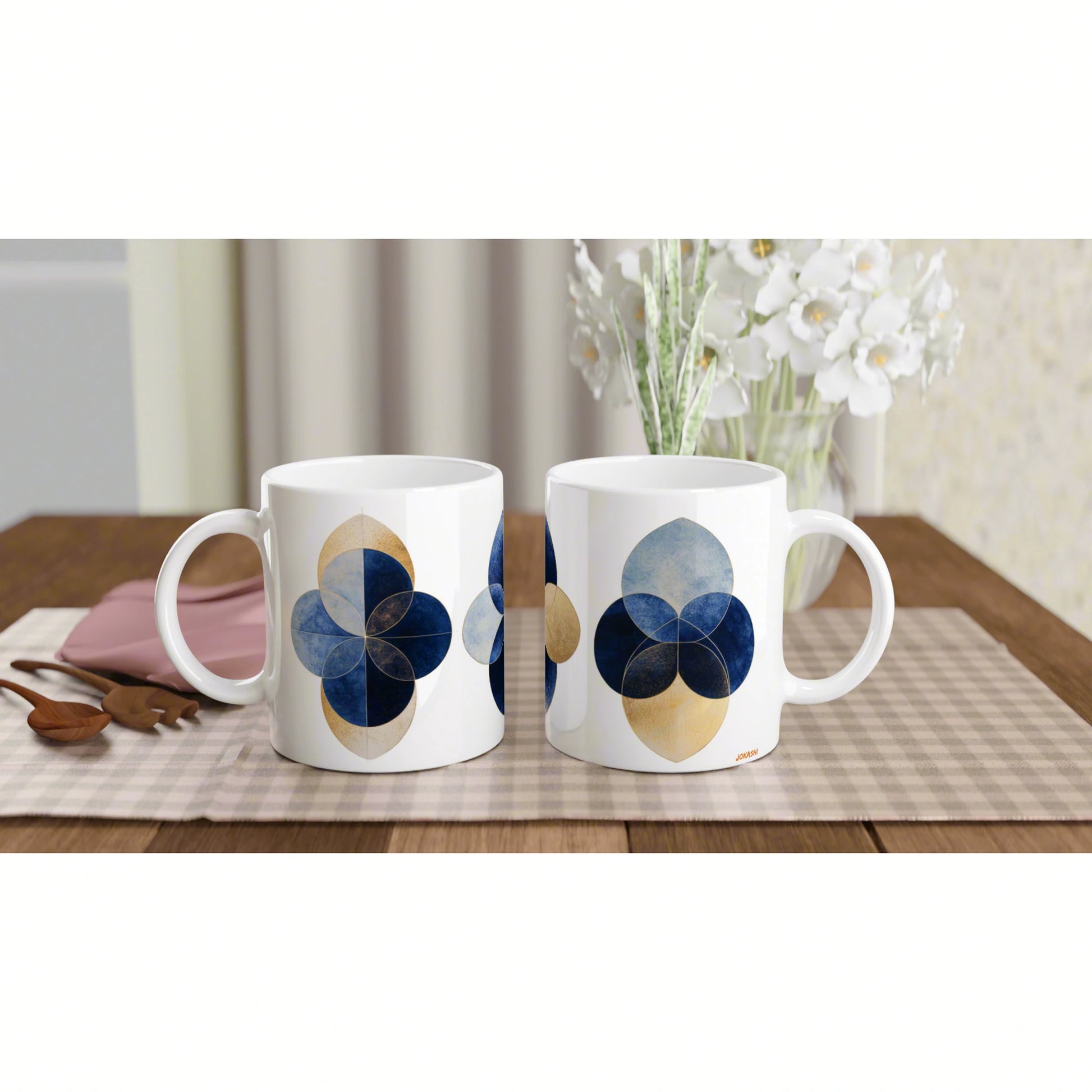 Two white mugs with blue and gold geometric quatrefoil patterns, shown as a product mockup on a checkered placemat.