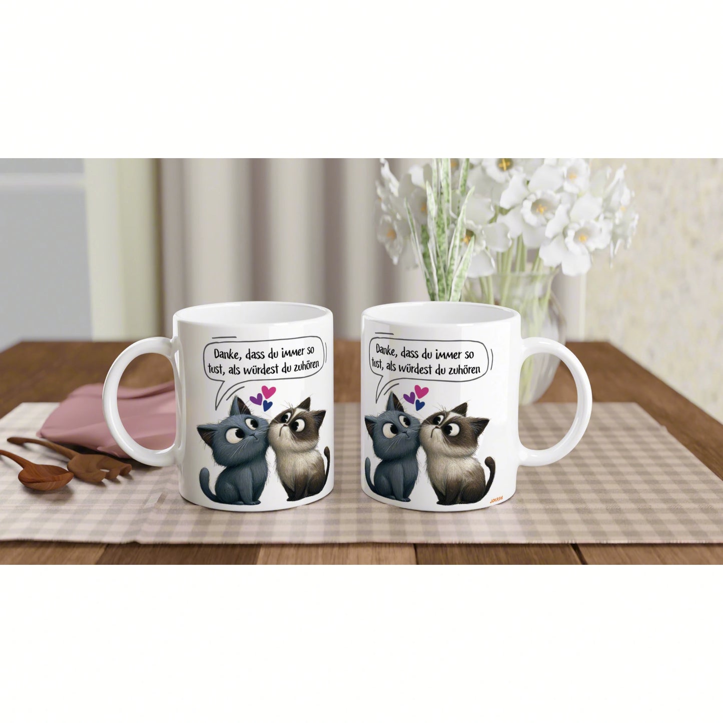 Two white mugs with cartoon cats facing each other and a German speech bubble, on a wooden table with flowers (product mockup).